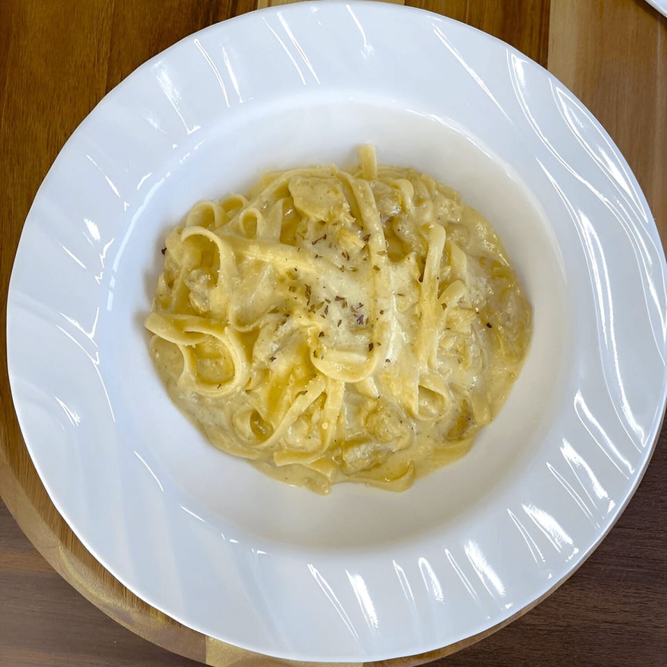 Creamy fettuccine pasta with herbs and cheese in a white bowl on a wooden table.
