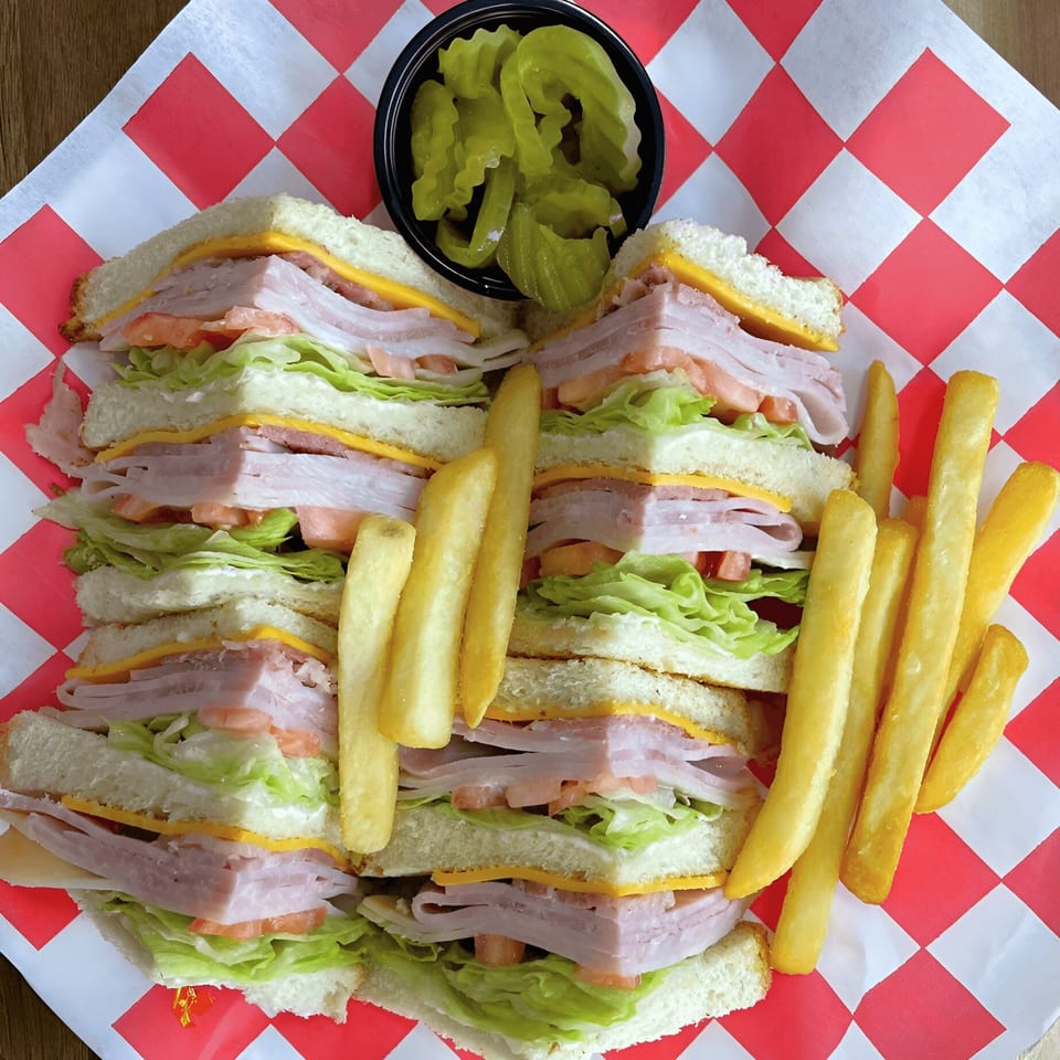 Club sandwich with fries and pickles on red and white checkered paper from Flip Pizza and Grill.
