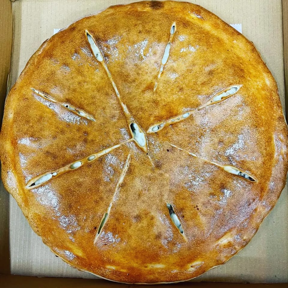 A golden-brown calzone with steam vents, dusted with flour, in a cardboard pizza box.