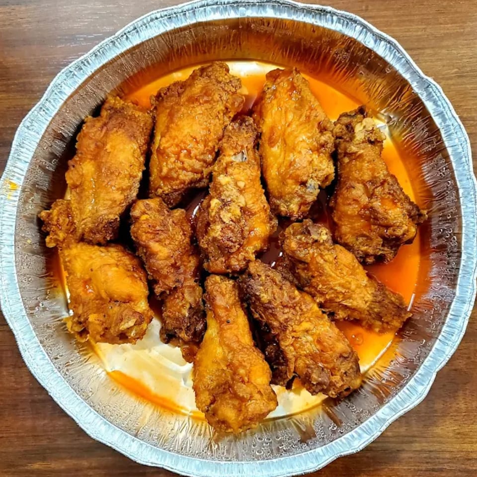 Crispy fried chicken wings coated in a vibrant orange sauce, served in a round foil pan.